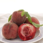 rotfleischiger Pfirsich der Sorte Ellora auf dem Teller, aufgeschnitten